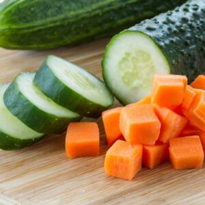 Sliced cucumbers and diced carrots on a wooden cutting board.