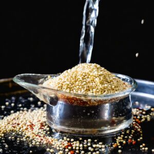 Rinsing quinoa in a glass bowl under a stream of water.