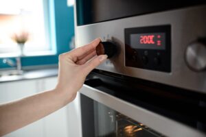 Setting the oven temperature to 200 degrees Celsius for baking, a person's hand is adjusting the modern oven's control knob, with the digital display showing the set temperature