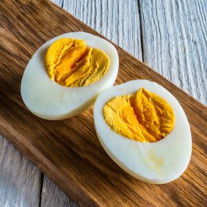 Two halves of a perfectly boiled egg with vibrant yellow yolks, resting on a wooden cutting board.