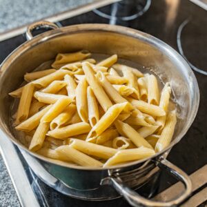 A colander filled with freshly boiled gluten-free penne pasta, steaming over a stove, ready for a delicious pesto mix to create Gastritis-Friendly Gluten-Free Pasta.