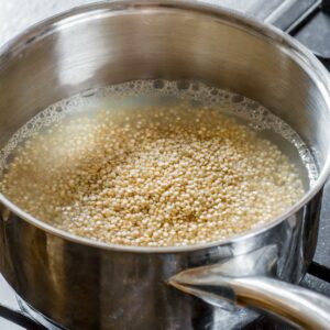 A pot on the stove with quinoa grains just beginning to cook in bubbling water, representing the initial phase of quinoa preparation where it transforms from raw to a fluffy, edible grain.