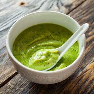 A white bowl filled with a creamy green avocado dressing, with a spoon lifting some of the thick mixture, showcasing the smooth and blended consistency perfect for drizzling over a fresh salad.