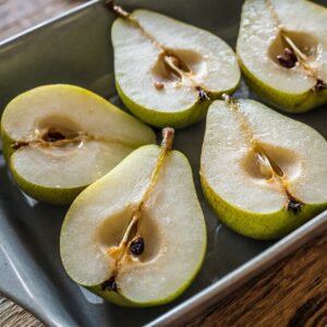 Halved pears with cores removed, neatly arranged cut-side up on a stainless steel baking tray, showcasing their fresh and juicy interior ready for seasoning.