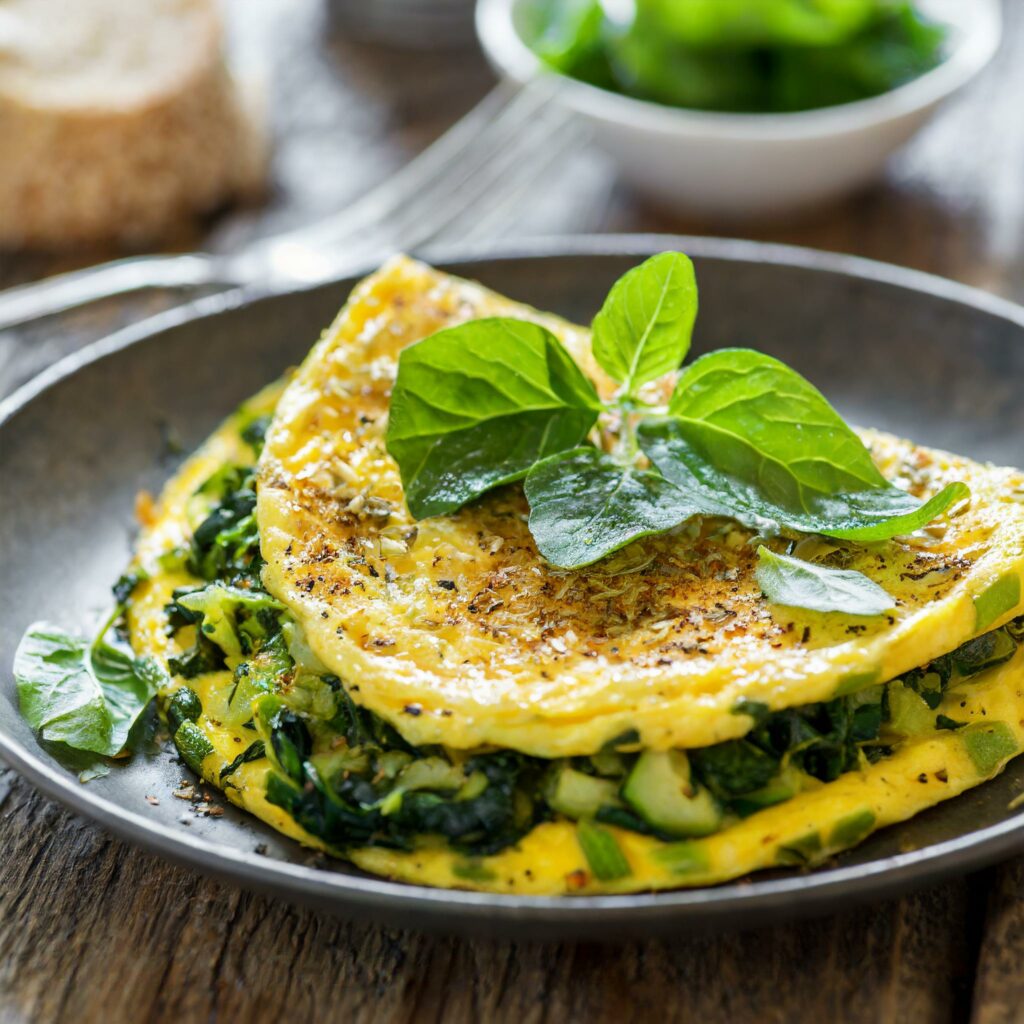 A warm, golden Gastritis-Friendly Spinach and Fennel Omelette folded neatly on a rustic plate, showcasing a vibrant filling of cooked spinach, grated zucchini, and finely chopped fennel, garnished with fresh basil leaves on top, ready for a gastritis-friendly breakfast feast.