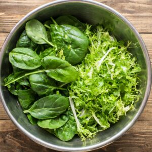 A bowl of vibrant green mixed salad leaves, with fresh spinach making up half of the mix, and crisp green lettuce comprising the other half, ready for additional salad ingredients.