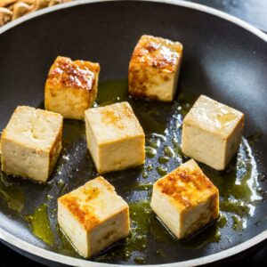 Golden-browned tofu cubes sizzling in olive oil, perfectly seared on all sides to a crispy exterior, ready for the next flavorful stir-fry ingredients.