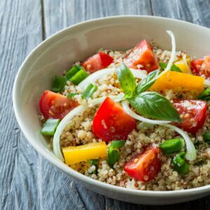 A bowl of freshly mixed ingredients with fluffy quinoa, crisp bell peppers, leek, juicy tomatoes, and a hint of oregano, all brought together with a drizzle of olive oil and a pinch of sea salt, ready for stuffing.