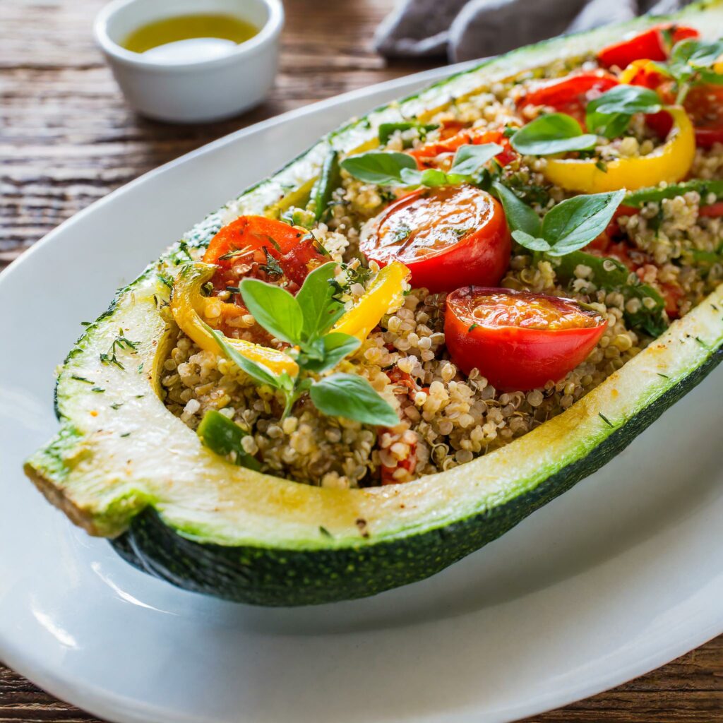 A vibrant and hearty Quinoa and Vegetable Stuffed Zucchini boat, garnished with fresh basil on a white plate, showcasing the colorful quinoa, bell peppers, leek, and cherry tomatoes filling.