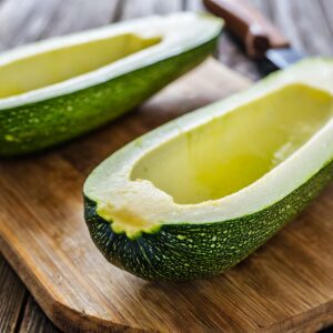 Fresh zucchini halves on a wooden cutting board, hollowed out carefully to form perfect boats, ready to be filled with nutritious ingredients