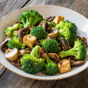 A delectable Gluten-Free Tofu and Mushroom Stir-Fry, featuring golden tofu cubes, sautéed mushrooms, and vibrant broccoli florets, all beautifully tossed with savory Bragg liquid aminos and aromatic cumin, ready to be savored.