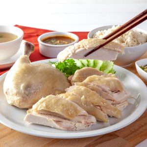 A platter of steamed chicken pieces alongside a bowl of clear soup, a side of rice, and condiments, showcasing a balanced and nutritious steamed meal, perfect for a gastritis-friendly diet.